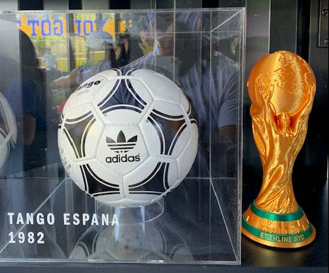 Gold World Cup trophy 3D print displayed next to a vintage soccer ball exhibit