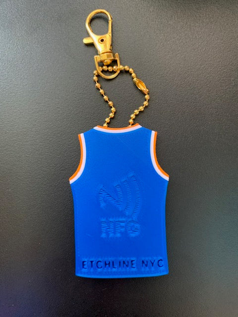 Back of personalized Knicks jersey keychain with NFC tap symbol and Etchline NYC maker mark with gold ball bead chain and lobster claw clasp on a dark gray background.