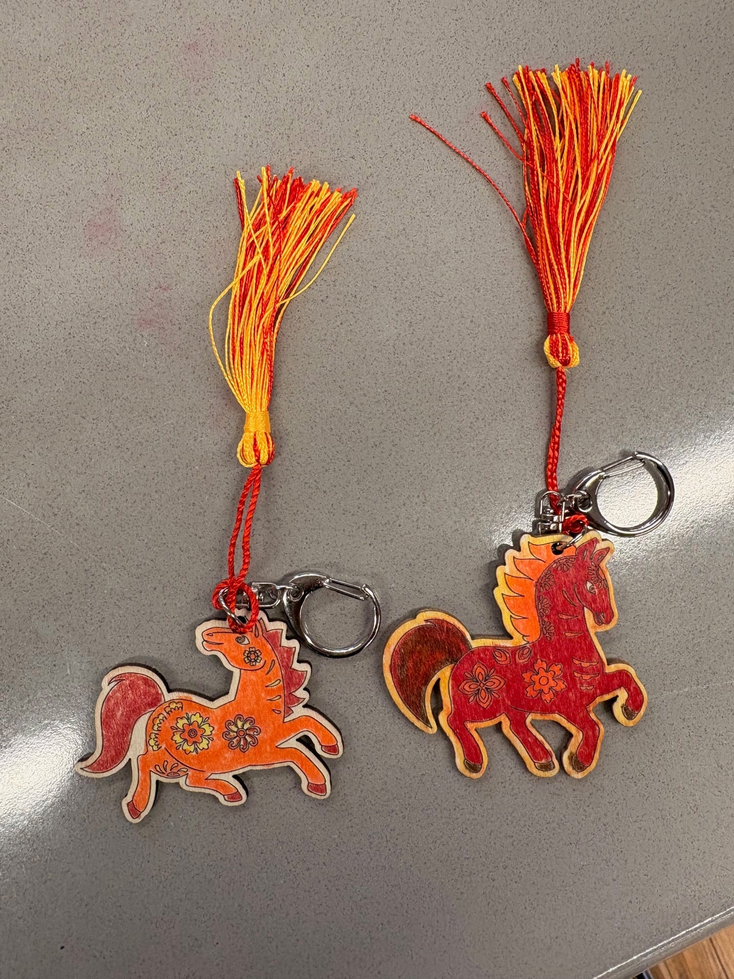 Two red and orange keychains with tassels on a school desk after the children colored it in.