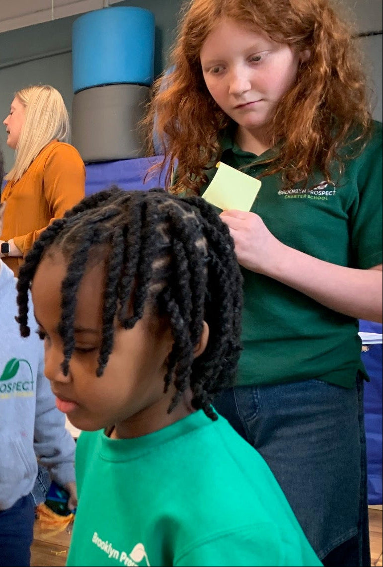 Children and adults in a classroom setting watching the laser machine etch their customized keychain.
