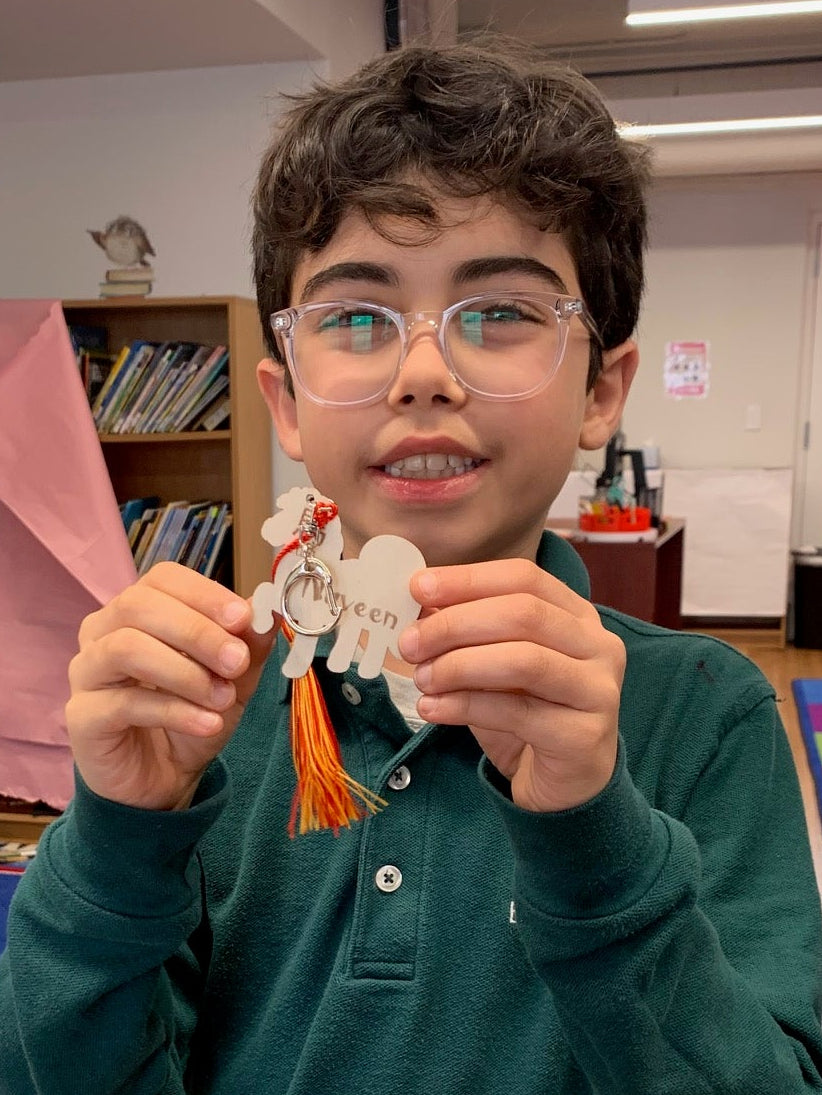 Child holding a laser engraved keychain with his name on it in a room with colorful rug and furniture.
