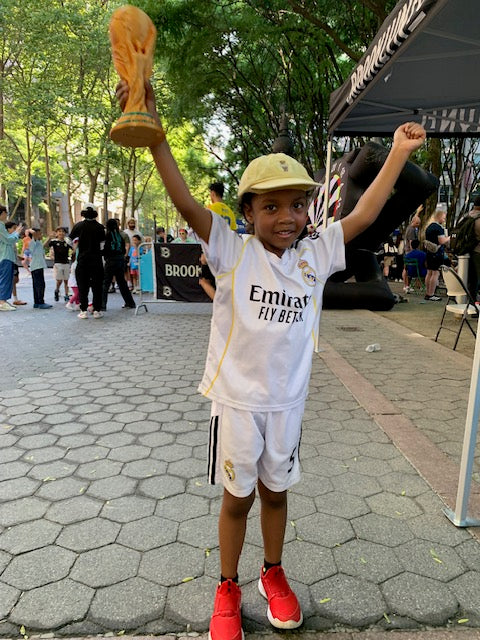Young soccer fan holding an Etchline 3D printed gold soccer trophy at Kids Soccer Village at Brooklyn Commons
