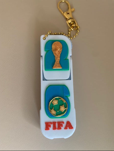 FIFA World Cup phone holder fidget keychain folded flat with gold-tone keychain hardware, trophy, soccer ball, and FIFA details.