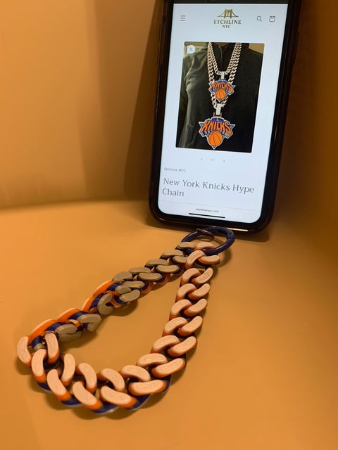 On the phone is a matching New York Knicks colors Hype Chain wristlet connected with a blue o-ring carabiner. The cell phone screen shows the EtchlineNYC.com website page of the New York Knicks Hype Chain.