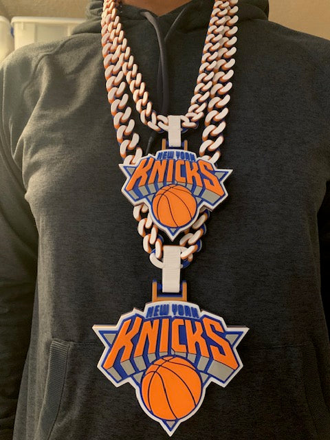 Man wearing black hoodie with two New York Knicks chain on.  One in kids size and the other in adult size.