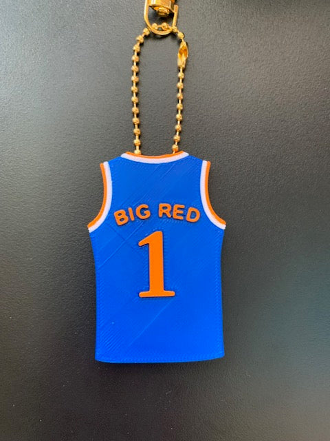 A Knicks basketball jersey-shaped keychain with orange text 'BIG RED' on the back, and the number '1', attached to a gold ball chain on a dark gray background.